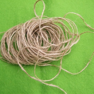 Könnte beinhalten: Ein Knäuel aus natürlichem Bindfaden aus Jute, auf einer grünen Oberfläche aufgerollt. Der Bindfaden ist hellbraun und hat eine raue Textur.