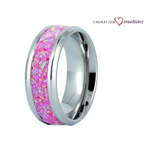 May include: A stainless steel ring with a pink opal inlay. The ring is a cremation ring, which means it can hold a small amount of ashes or other mementos. The ring is a beautiful and unique way to remember a loved one.