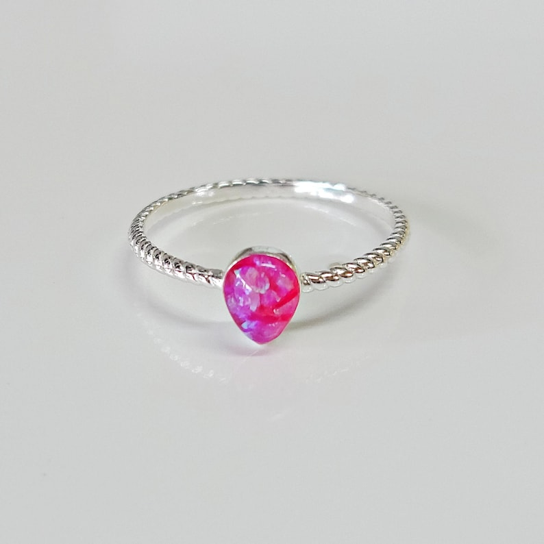 May include: A silver ring with a pink opal teardrop-shaped stone. The ring band is twisted.