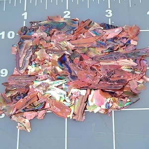 May include: A pile of iridescent pink and green abalone shell pieces. The shell pieces are various sizes and shapes.