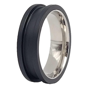 May include: A black and silver ring with a wide band and a beveled edge. The ring is made of two materials, with a black rubber outer band and a silver metal inner band.