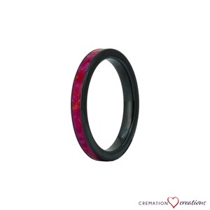 May include: A black ceramic ring with a thin band of pink opal inlay. The ring is a simple design with a smooth finish.