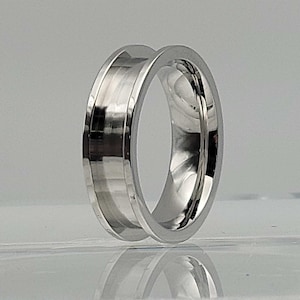 May include: A silver ring with a wide band and a grooved design. The ring is made of metal and has a polished finish.
