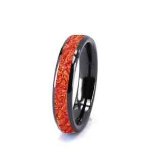 May include: A black tungsten carbide ring with a thin orange inlay. The inlay is made of crushed opal.