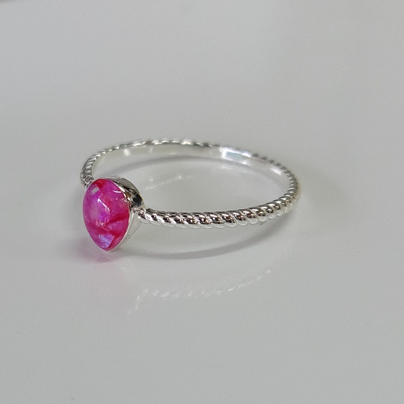 May include: A silver ring with a pink opal gemstone. The band is twisted and has a rope-like design.