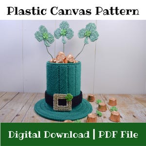 May include: A green plastic canvas leprechaun hat with a black band and a gold buckle, holding shamrock decorations and chocolate coins. The text "Plastic Canvas Pattern" and "Digital Download | PDF File" are displayed.