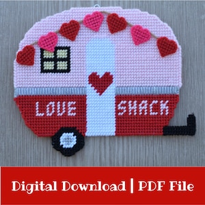 May include: A handmade, pink and red camper-shaped wall hanging with the words "LOVE SHACK" stitched across the bottom. The camper features a garland of heart-shaped decorations and a heart on the front.