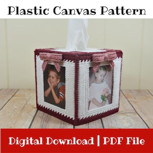 May include: A handmade tissue box featuring a plastic canvas pattern. The box is white with burgundy trim and decorative bows. It has two photo frames with pictures of children. The text "Plastic Canvas Pattern" and "Digital Download | PDF File" are visible.