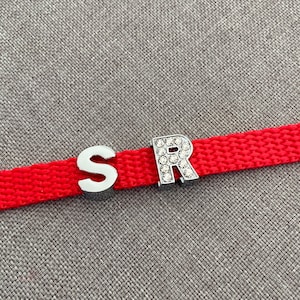 Pode incluir: Tecido vermelho com pingentes de letras prateadas que soletram "SR" com strass na "R".