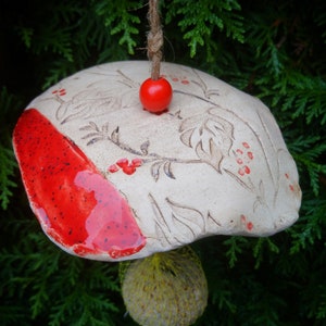 Pode incluir: Carrilhão de vento de cerâmica branca em forma de cogumelo com um esmalte vermelho em um lado. O cogumelo tem um design floral e uma conta vermelha no topo.
