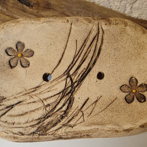 Può includere: Un portasapone in ceramica con una glassa marrone chiaro e un design di linee nere e due fiori gialli. Il portasapone ha due fori di scarico.