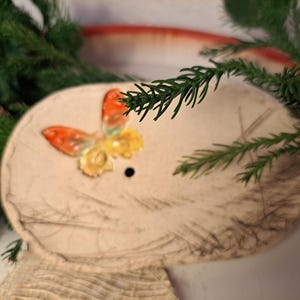 Peut inclure: Un porte-savon ovale de couleur crème avec un motif de papillon en relief orange, jaune et vert. Le porte-savon a un petit trou de drainage et est entouré d'aiguilles de pin vertes.