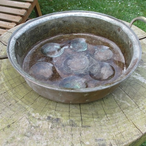 Può includere: Una pentola di rame vintage con due manici e un interno testurizzato. La pentola ha un aspetto usurato e invecchiato e sembra essere stata usata.