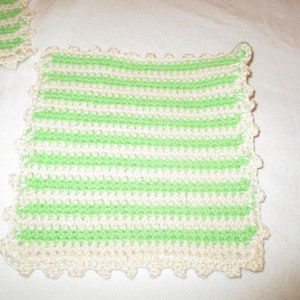 Könnte beinhalten: Nahaufnahme von zwei handgefertigten Topflappen aus Häkelarbeit. Die Topflappen weisen abwechselnd horizontale Streifen in Hellgrün und Off-White auf. Die Kanten sind mit einem gewellten Rand in Off-White versehen.