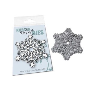 Könnte beinhalten: Eine Metallstanze in Form einer Schneeflocke mit einem Stern in der Mitte. Die Stanze befindet sich auf einer weißen Karte mit dem aufgedruckten Text "Karten Kunst Dies".