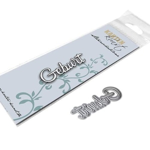 Op de afbeelding: Een pakket met een gestanst metalen woord, "Geburt", met een witte omtrek, en een kleiner gestanst woord, "Twinde". De verpakking heeft een lichtblauwe achtergrond met een bloemenontwerp en tekst.