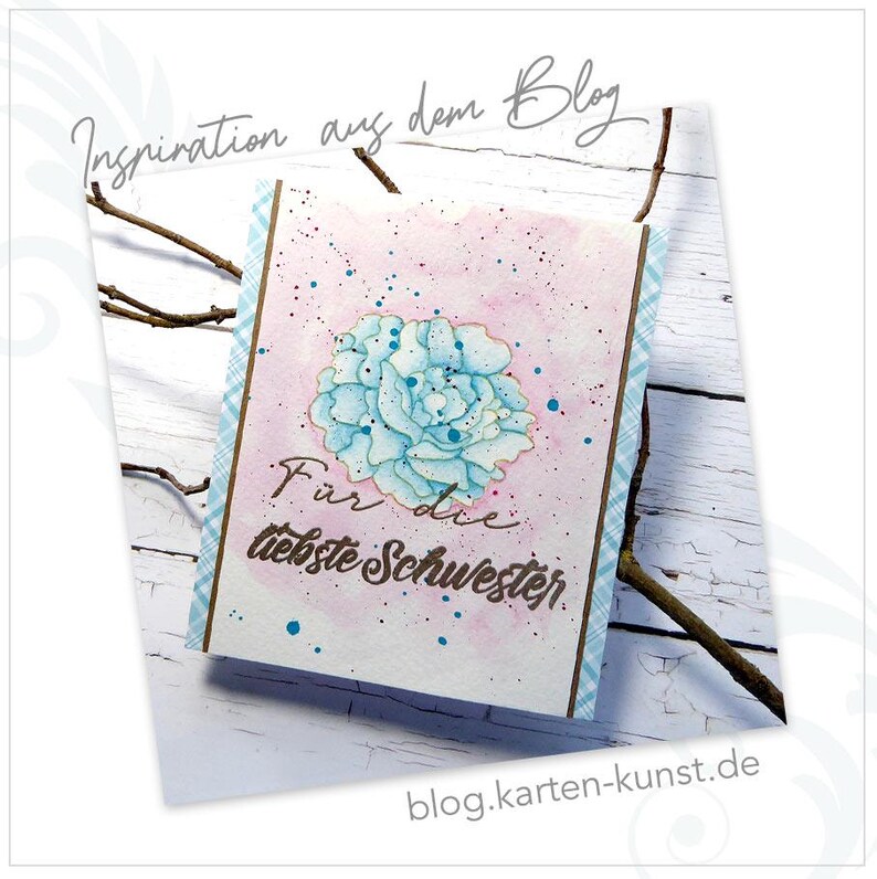 May include: A pink watercolor card with a blue flower and the text "For the dearest sister" in brown lettering. The card has a plaid border.