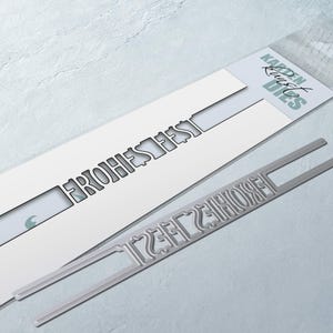 Könnte beinhalten: Eine Metallstanze zum Basteln mit dem deutschen Spruch "Frohes Fest". Die Stanze ist in einem durchsichtigen Plastikbeutel mit einem weißen Etikett verpackt, auf dem "Kaufen Rust Dies" steht.