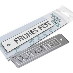 May include: A silver metal die cut with the text "Frohes Fest" in a rectangular shape. The die cut is on a white background with a floral pattern.