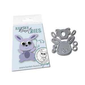 May include: A die-cut set with a cartoon bunny design, and a package with a matching illustration. The package has the text "Karten Kunst Dies" and a website address. The die-cut is silver-coloured.