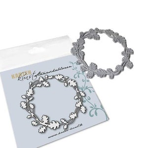 May include: A silver metal die cut of a wreath made of oak leaves. The die cut is on a white background with the text "KARDEN Kunst Stanzen" and a website address.