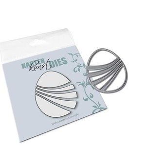 May include: A silver metal die-cut craft tool in the shape of a stylized sun or flower. The die has a circular outline with curved lines inside. The packaging features a matching design and the text "Karten Kunst Dies".