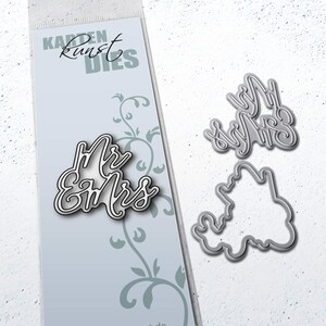 May include: A set of three metal die-cut stencils for crafting. The stencils feature the words "Mr & Mrs" in a cursive font. The stencils are on a white background with a blue and white patterned card behind them.