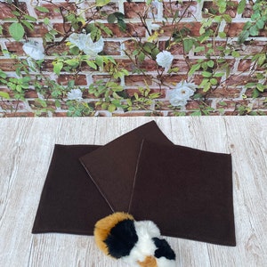 Könnte beinhalten: Drei braune Fleece-Katzenmatten, übereinander gelegt, mit einem kleinen Stoffkatzenspielzeug im Vordergrund.