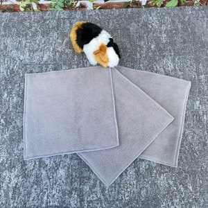 Könnte beinhalten: Drei graue Fleece-Tücher, die auf einer grauen, strukturierten Oberfläche gefaltet sind. Die Tücher sind weich und saugfähig.