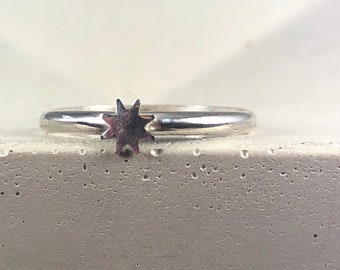 May include: A silver ring with a star-shaped design. The ring is simple and delicate.