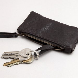 Könnte beinhalten: Ein brauner Leder-Schlüsselanhänger mit Reißverschluss und einem silbernen Schlüsselring mit daran befestigten Schlüsseln.