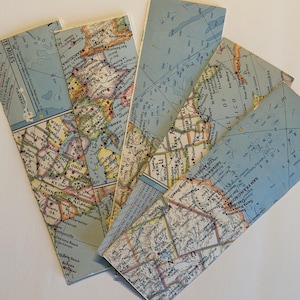 May include: A set of four rectangular bookmarks featuring printed sections of vintage-style maps. The designs display various geographic regions, including parts of the United States, Europe, and the Gulf of Mexico, with blue oceans and detailed land topography.