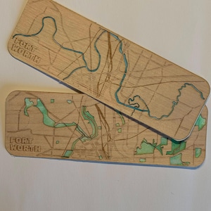 May include: Two rectangular wooden bookmarks featuring laser-engraved street maps of Fort Worth. The designs include etched road lines and recessed areas filled with a light green color, with the text FORT WORTH engraved on each piece.