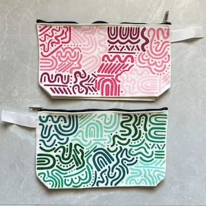 May include: Two zippered pouches with abstract patterns. The top pouch has a pink, white, and purple pattern. The bottom pouch has a green and blue pattern.