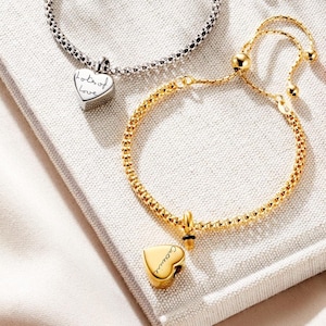 Pode incluir: Três pulseiras ajustáveis em prata, ouro e ouro rosa. Cada pulseira apresenta uma corrente delicada e um berloque em forma de coração com as palavras "lots of love" ou "love you" gravadas. As pulseiras são exibidas em uma superfície branca.