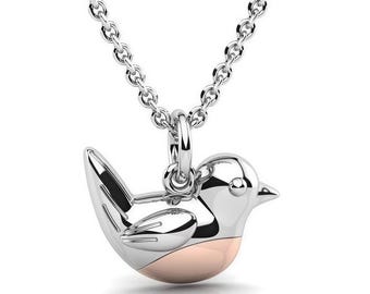 Könnte beinhalten: Eine silberfarbene Metallhalskette mit einem vogelformigen Anhänger. Der Anhänger hat einen polierten silbernen Kopf, Flügel und Schwanz sowie einen glatten, abgerundeten roségoldfarbenen Bauch. Er hängt an einer feinen silberfarbenen Gliederkette.