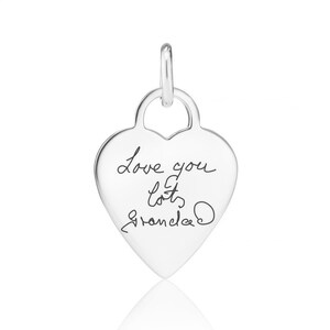 A silver heart-shaped charm with the handwritten message "Love you Grandma" engraved on it.