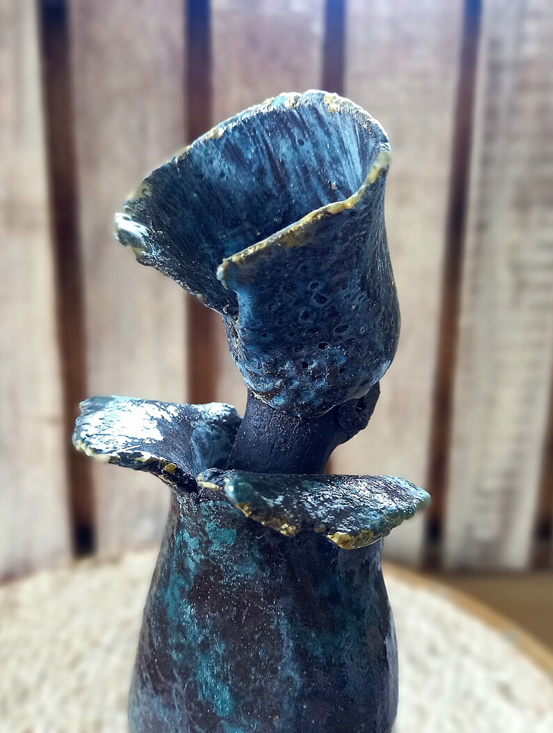 May include: A ceramic vase with a blue and green glaze and gold accents. The vase is shaped like a flower with a wide opening at the top.