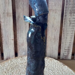 May include: A ceramic sculpture of a person wearing a tall, blue hat and a long, dark blue robe with gold accents. The sculpture has a textured, aged look.