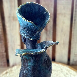 May include: A ceramic sculpture of a person with a blue and gold head and a blue and green body.