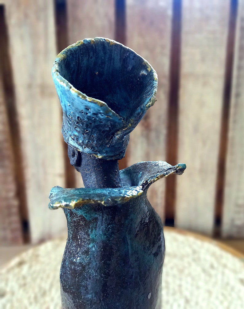 May include: A ceramic sculpture of a person with a blue and gold head and a blue and green body.