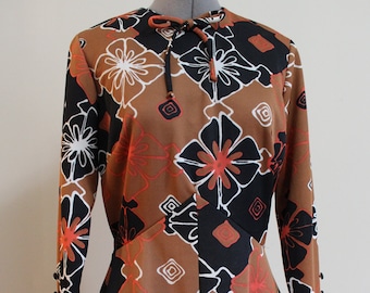 May include: A brown, black, and orange dress with a floral print. The dress has long sleeves and a tie at the neck.