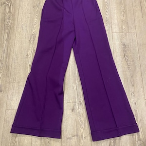 May include: A pair of vibrant purple wide-leg pants. The pants feature a high waist and a flared design, with a seam down the front of each leg. The hem is cuffed. The pants are made of a smooth, solid-colored fabric.