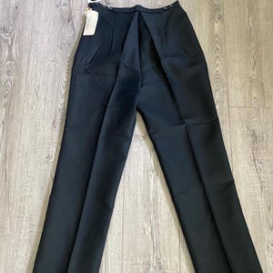 May include: Black dress pants with a straight leg design. The pants have a high waist and a button closure. A tag is attached to the pants. The pants are made of a smooth fabric.