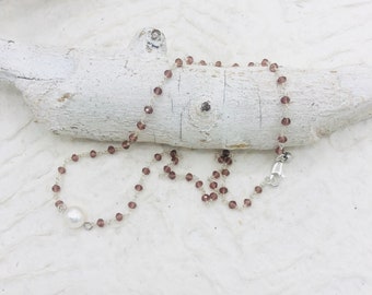 May include: A delicate silver chain necklace with small, dark purple glass beads and a single white pearl pendant.
