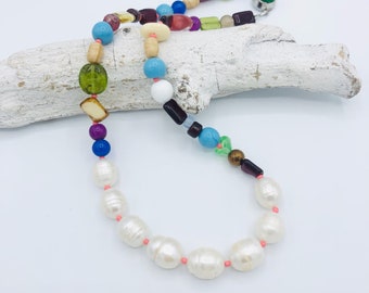 May include: A colorful beaded necklace with a variety of shapes and sizes. The necklace features a strand of large, white pearls with pink accents.