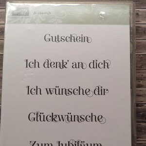 Op de afbeelding: Een set van vijf transparante rubberen stempels met Duitse tekst. De stempels bevatten de woorden "Gutschein", "Ich denk' an dich", "Ich wünsche dir", "Glückwünsche" en "Zum Jubiläum".