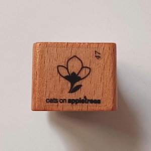 Op de afbeelding: Een houten stempel met een zwart-witte illustratie van een bloem. De stempel is gelabeld "cats on appletrees" en heeft het nummer 47 erop.