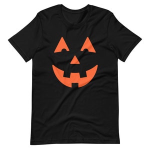 Puede incluir: Camiseta negra con un gr&aacute;fico de cara de calabaza naranja.
