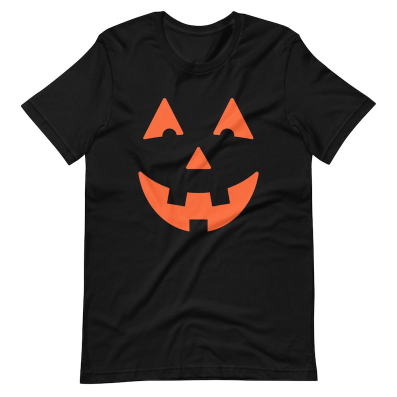Puede incluir: Camiseta negra con un gr&aacute;fico de cara de calabaza naranja.